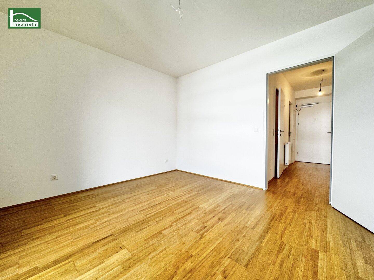 Geräumiger, heller Raum mit Holzboden und Zugang zum Flur, bereit zur individuellen Gestaltung.