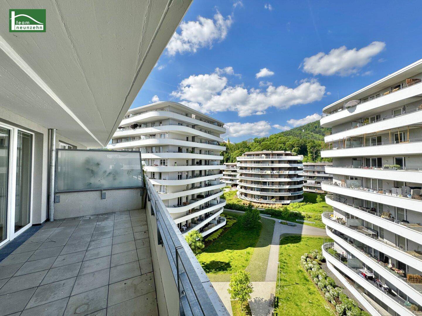 Geräumiger Balkon mit Blick auf moderne Wohngebäude, grüne Anlagen und die umliegende Berglandschaft.