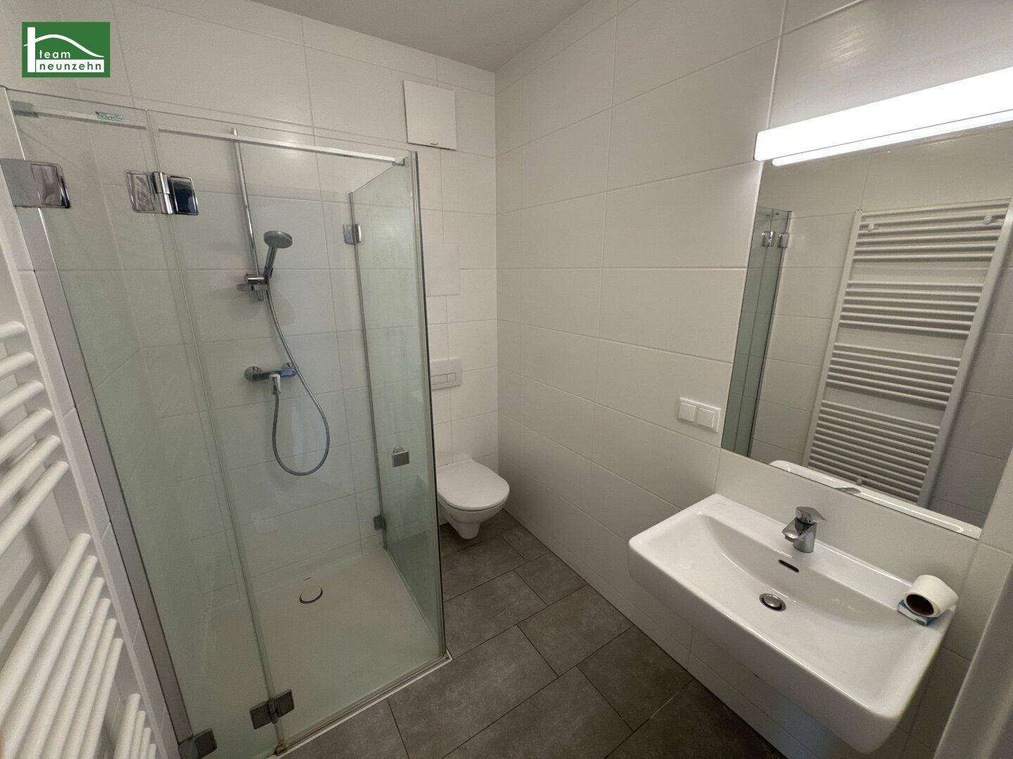 Modernes Badezimmer mit Duschkabine, wandhängendem WC, Waschbecken und beheiztem Handtuchhalter.