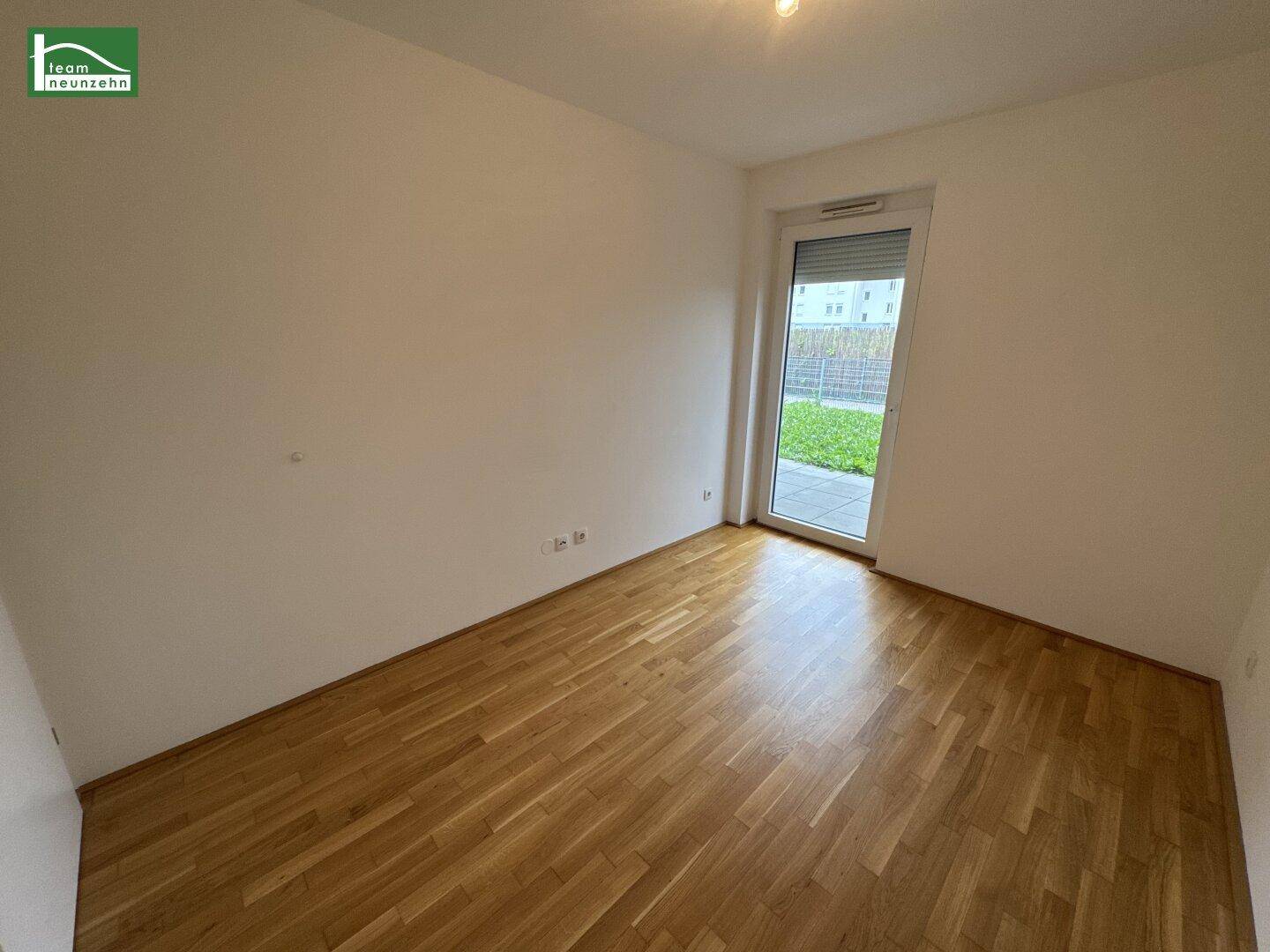 Leeres Schlafzimmer mit Parkettboden und direktem Zugang zu einem kleinen Gartenbereich.