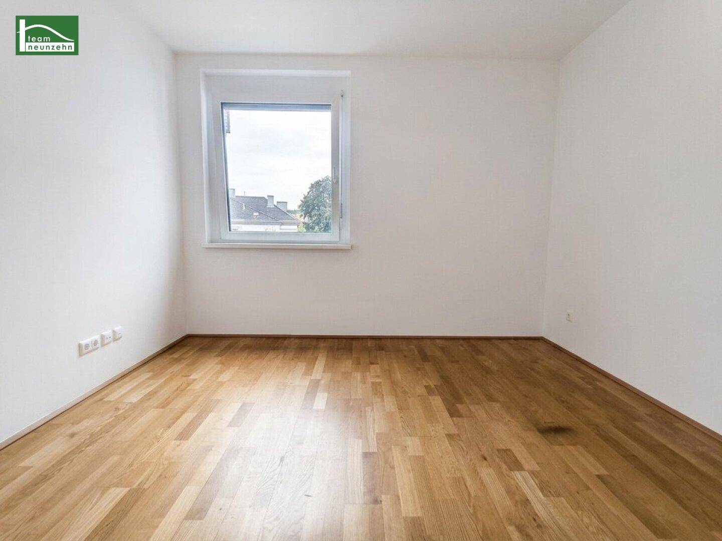 Helles Schlafzimmer mit Parkettboden und einem Fenster, das viel Tageslicht hereinlässt.