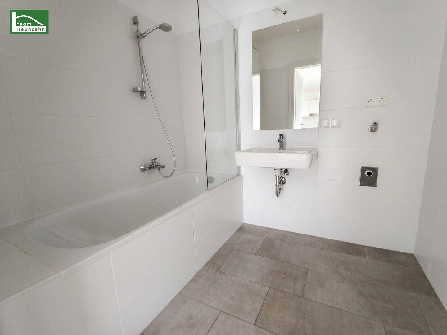 Modernes Badezimmer mit Badewanne, Duschfunktion, Waschbecken und hellen Fliesen.