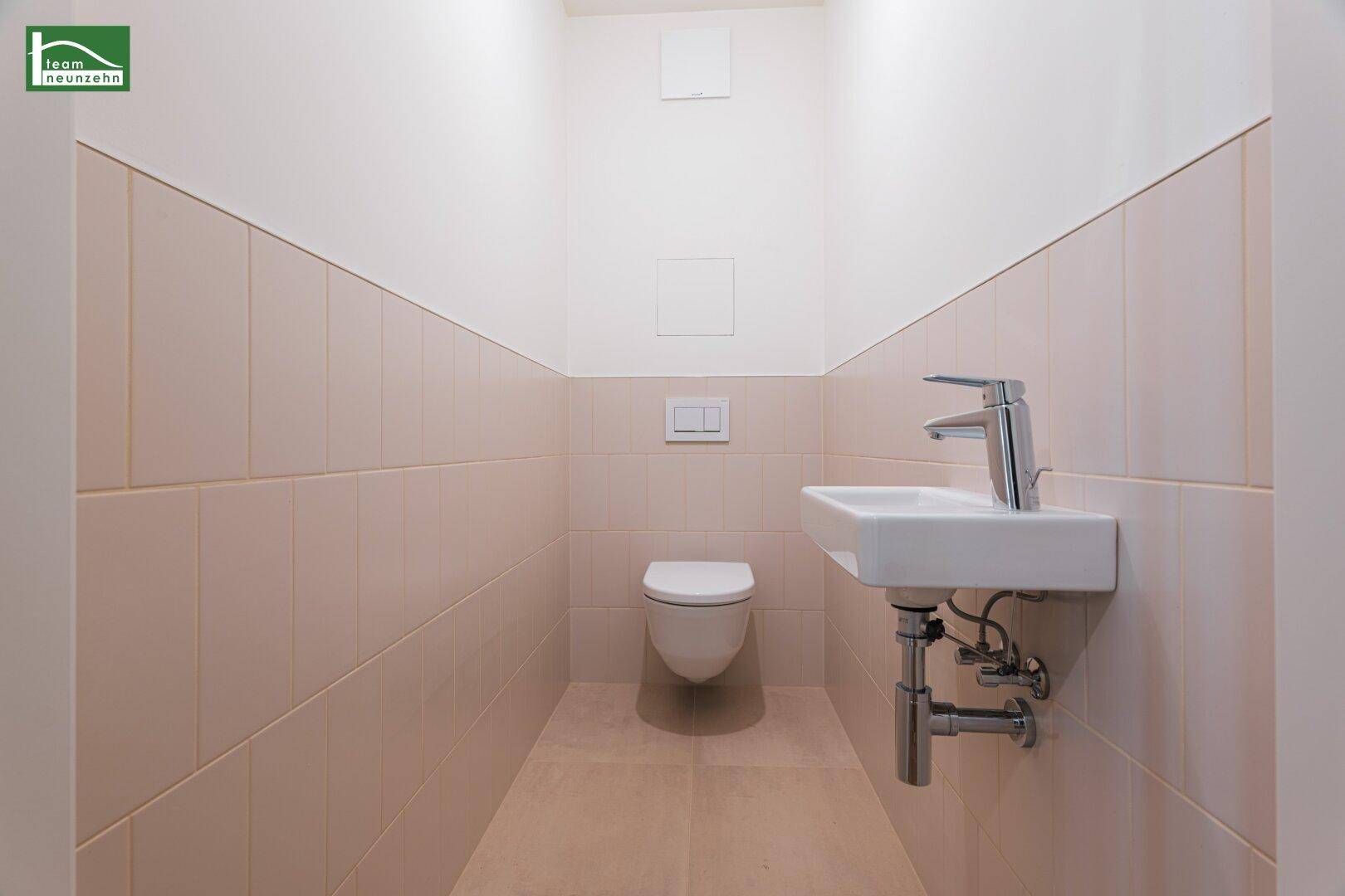 Modernes Gäste-WC mit Wand-WC und kleinem Waschbecken, hell gefliest und funktional gestaltet.