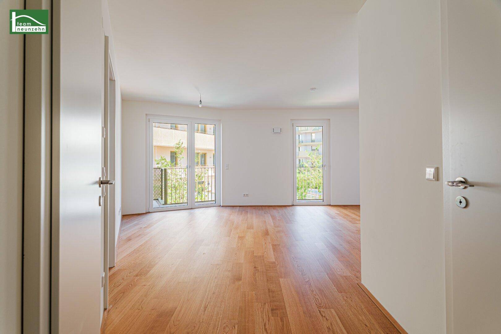 Geräumiges Wohnzimmer mit hellem Parkettboden und Zugang zu einem französischen Balkon, lichtdurchflutet.