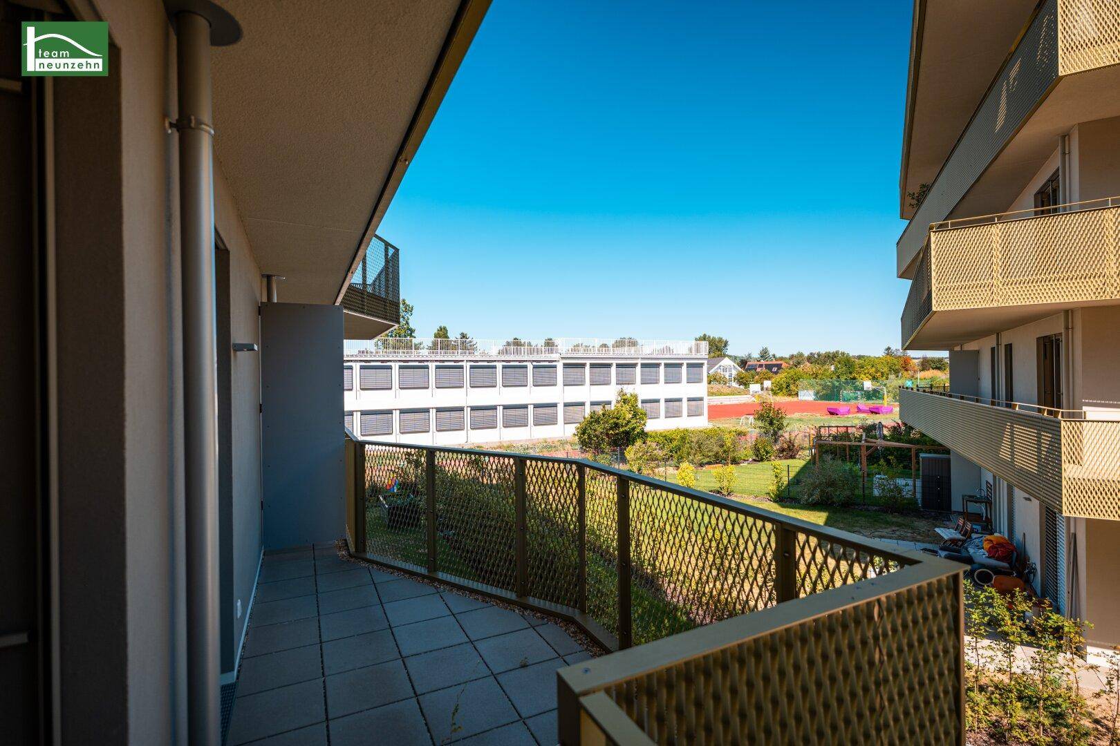 Geräumiger Balkon mit Fliesenboden und weitem Blick über die umliegende Grünfläche und Gebäude.