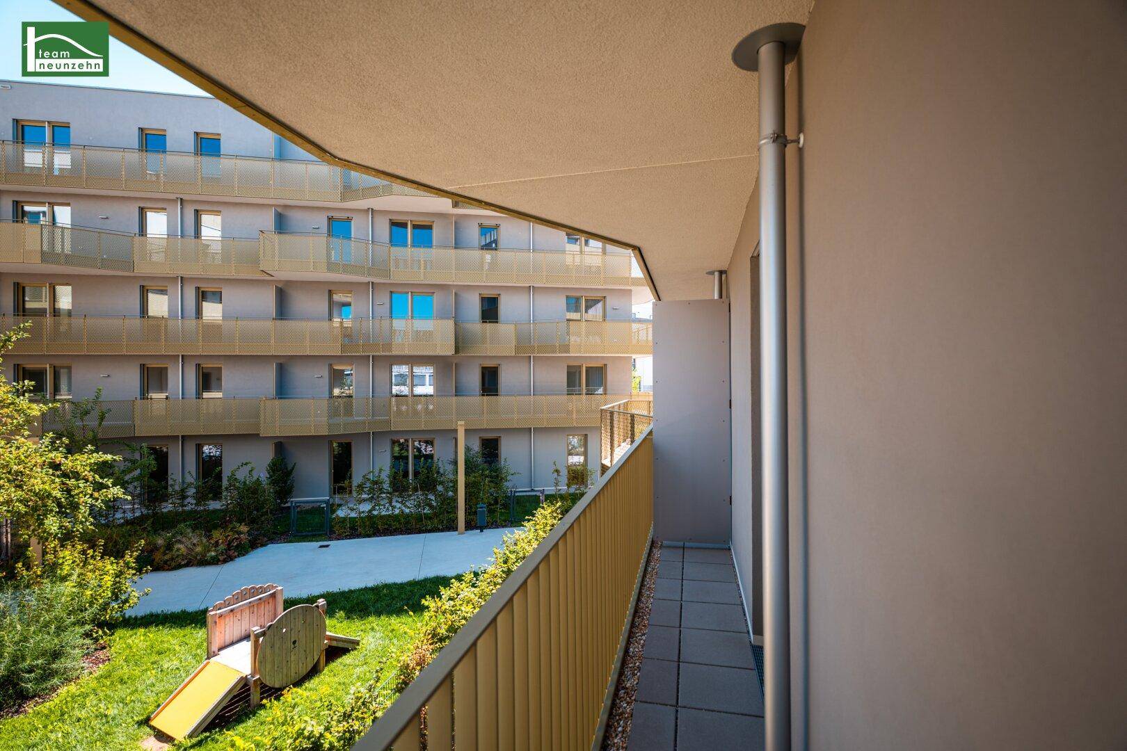 Balkon mit Blick auf den Gemeinschaftsgarten und Kinderspielplatz der modernen Wohnanlage.