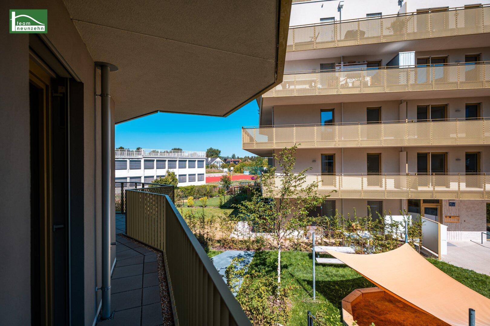 Heller Balkon mit Blick auf den gepflegten Gemeinschaftsgarten und die moderne Architektur des Gebäudes.