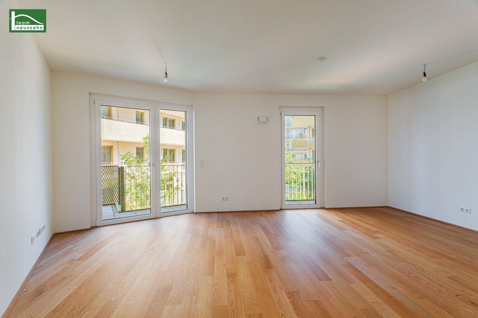 Lichtdurchfluteter Wohnraum mit Eichenparkett und Zugang zu einem kleinen Balkon mit Grünblick.