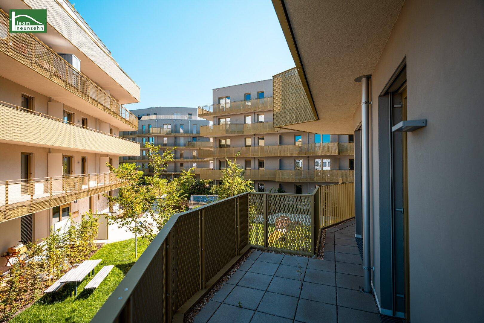 Moderner Balkon mit Blick auf den begrünten Innenhof und weitere Wohngebäude.