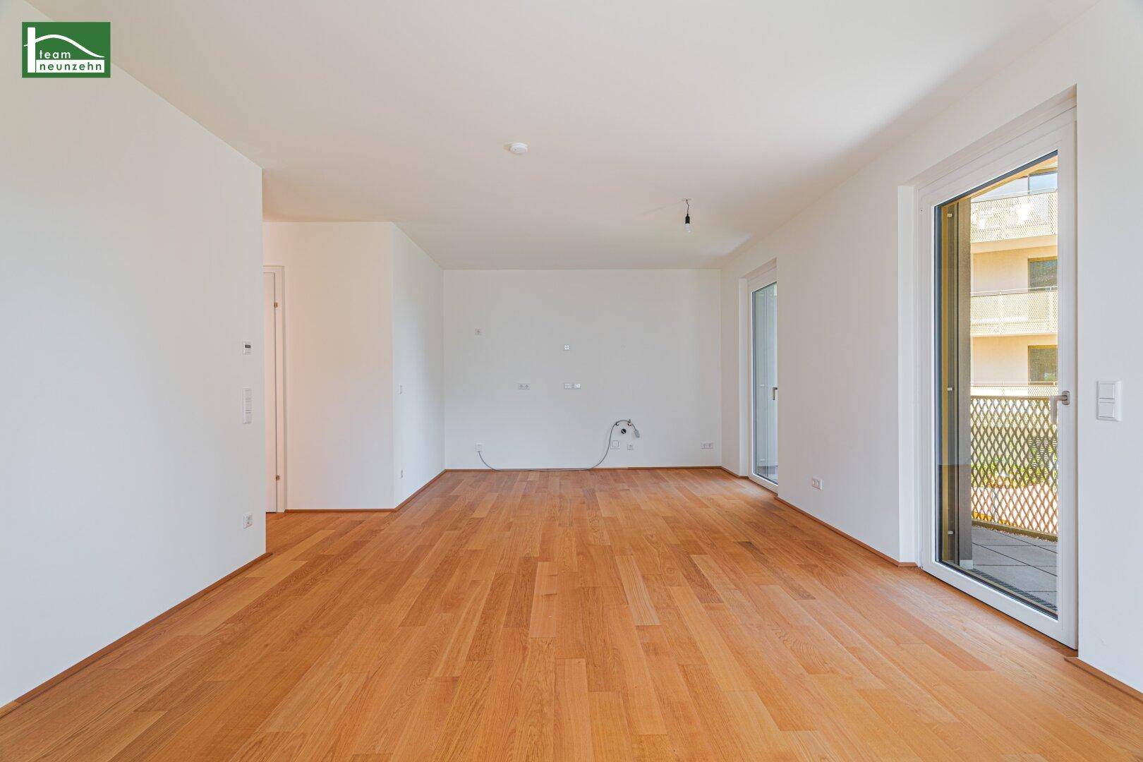Heller, leerer Raum mit Holzboden, weißen Wänden und Zugang zu einem Balkon.