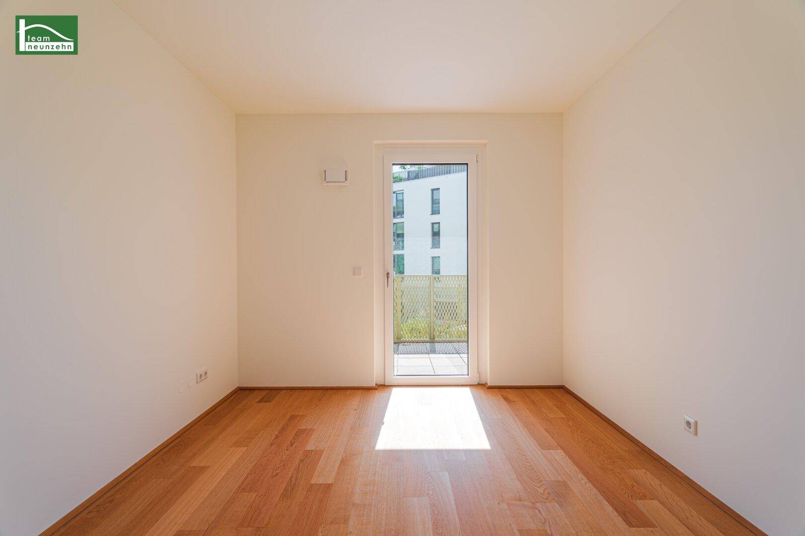 Helles Schlafzimmer mit Holzboden und Balkonzugang, durchflutet von natürlichem Sonnenlicht.
