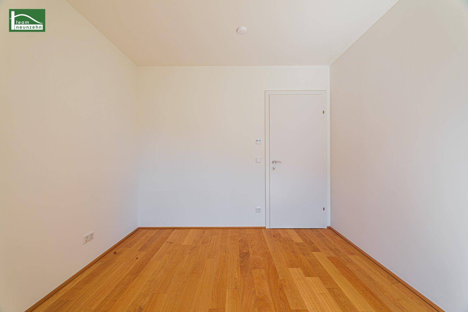 Leeres Schlafzimmer mit Holzboden und weißer Tür, bereit zur individuellen Gestaltung.