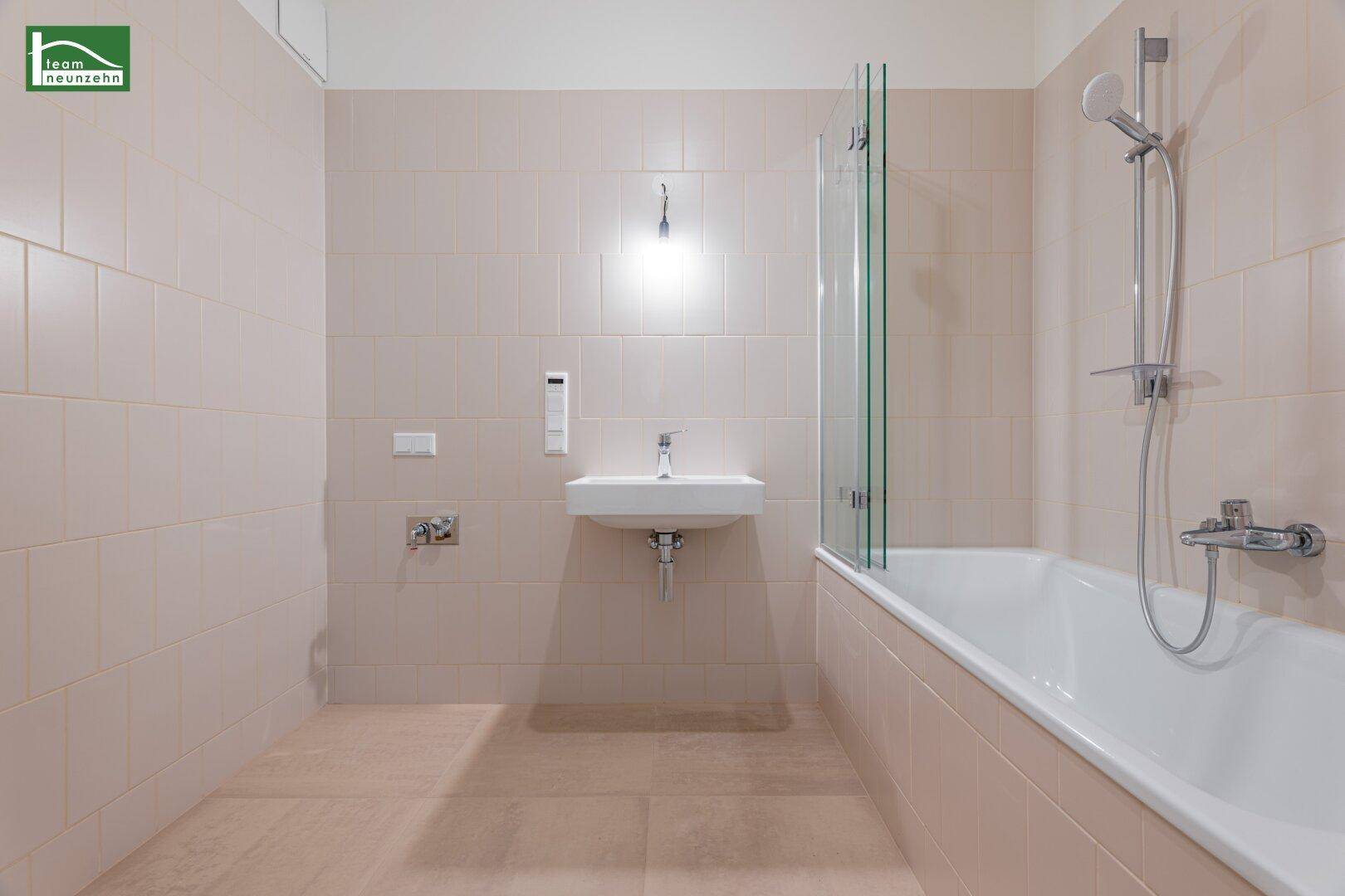 Modernes Badezimmer mit beigefarbenen Fliesen, Badewanne mit Duschwand und Einzelwaschbecken.
