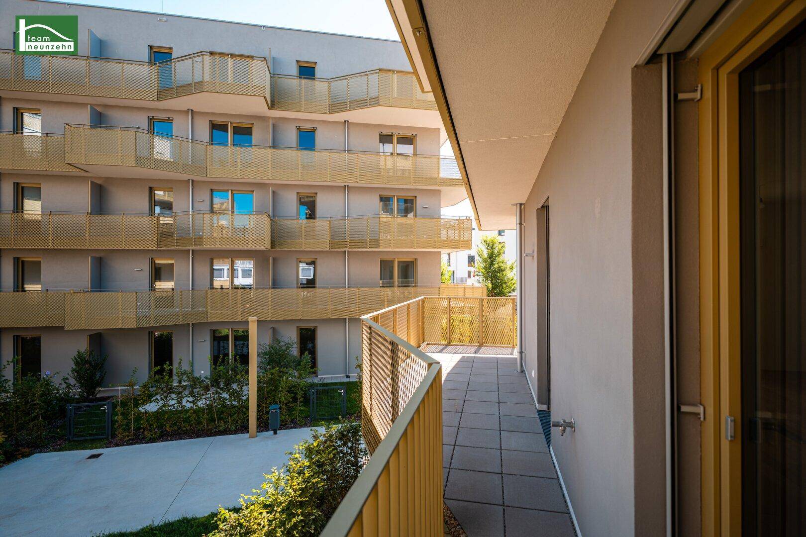 Langer Balkon mit Fliesen und modernem Geländer, mit Blick auf die gepflegte Außenanlage.