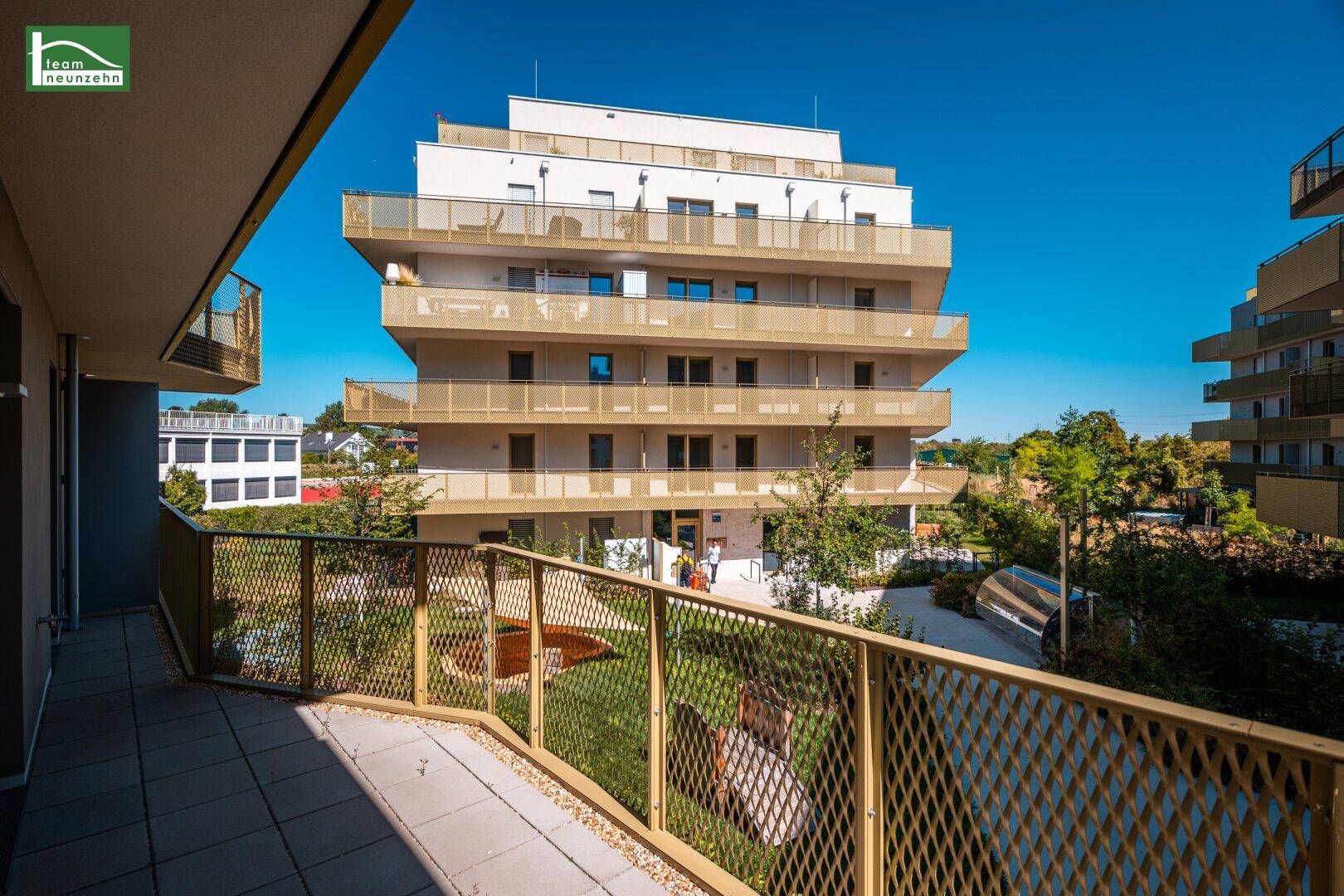 Balkon mit Fliesenboden und goldenem Geländer, bietet weiten Blick auf die moderne Wohnanlage.