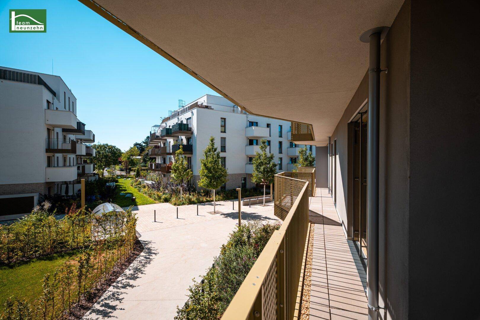 Geräumiger Balkon mit Fliesenboden und modernem Geländer, mit Blick auf den grünen Innenhof.