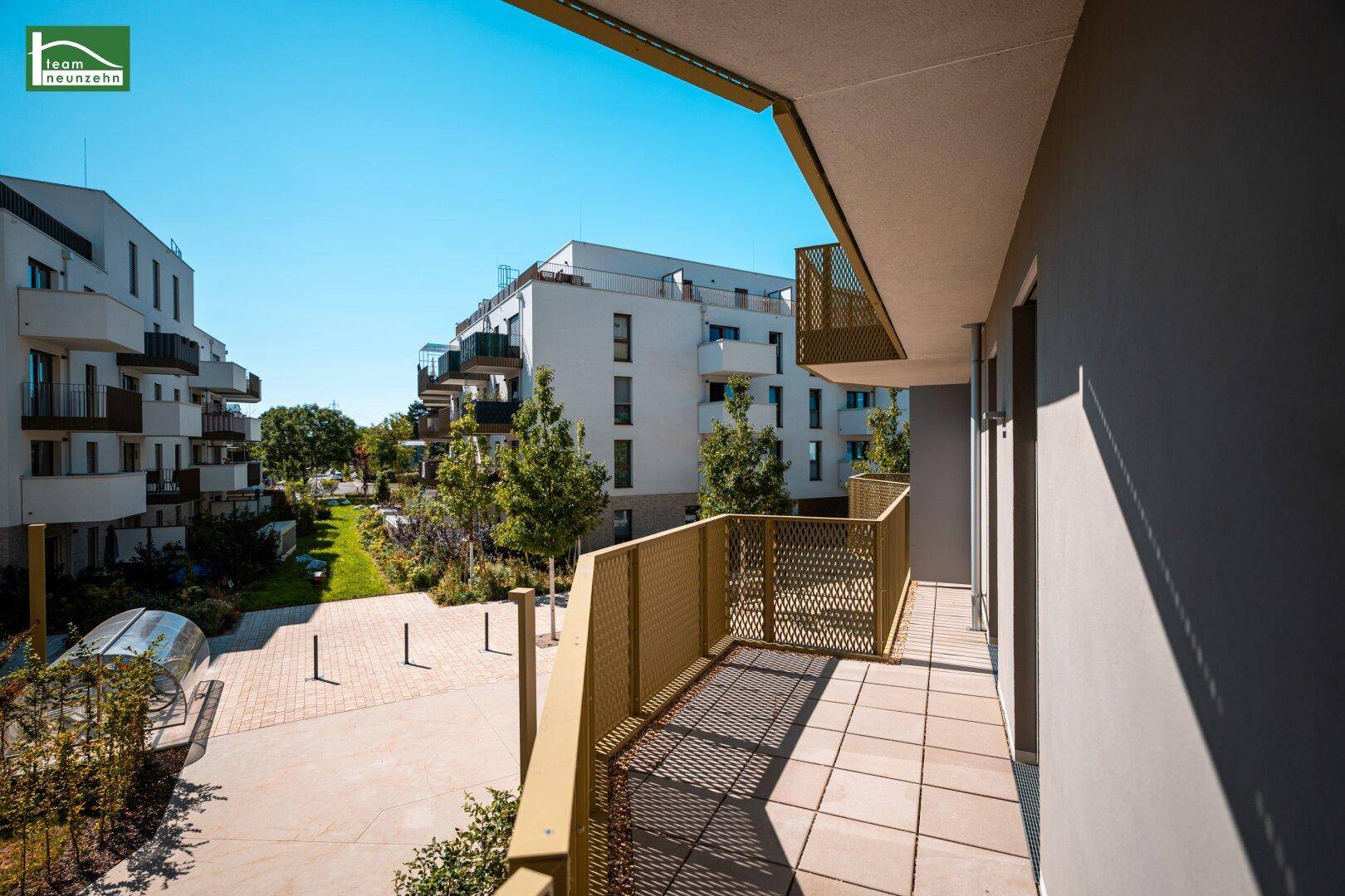 Langer Balkon mit Fliesenboden und Blick auf die gepflegte Außenanlage und weitere Neubauten.