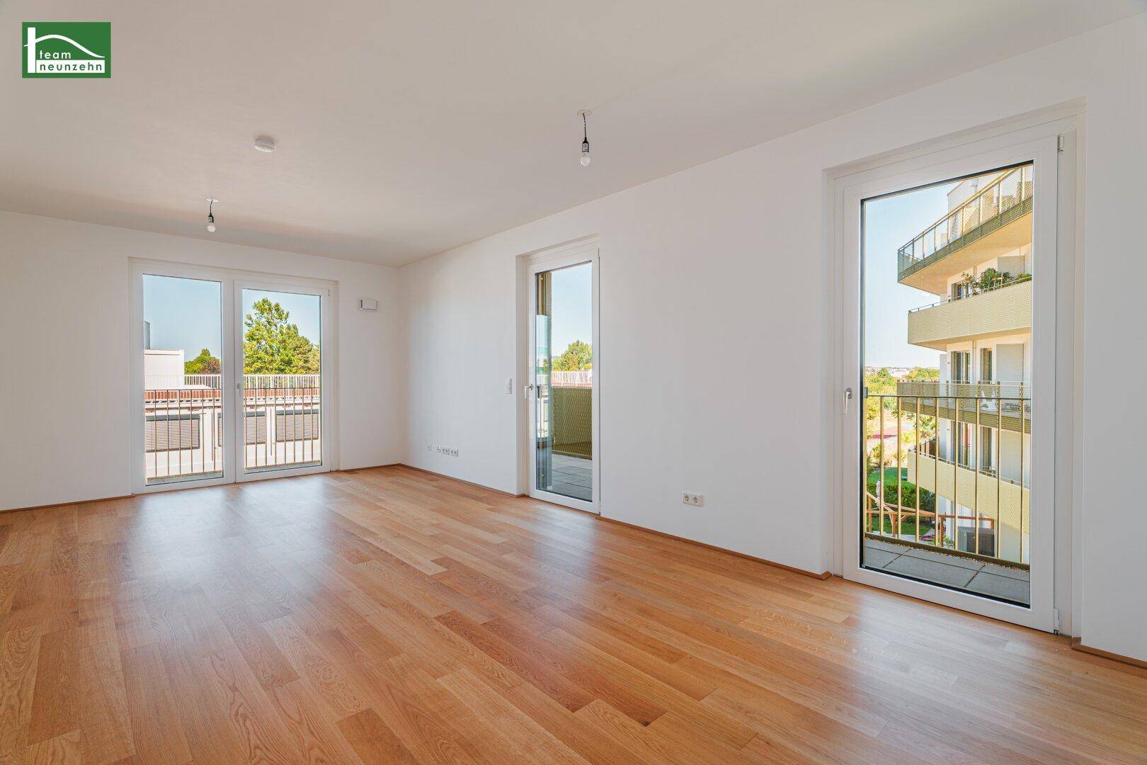 Helles Wohnzimmer mit Holzboden und Zugang zu mehreren Balkonen, bietet viel natürliches Licht.