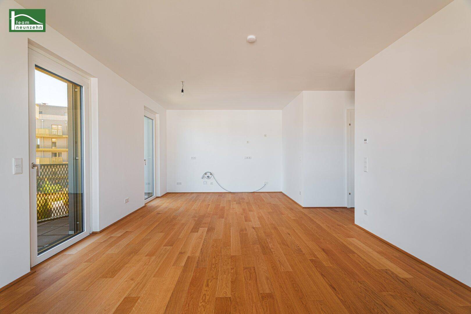 Geräumiges, leeres Wohnzimmer mit hellem Holzboden und weiß gestrichenen Wänden.