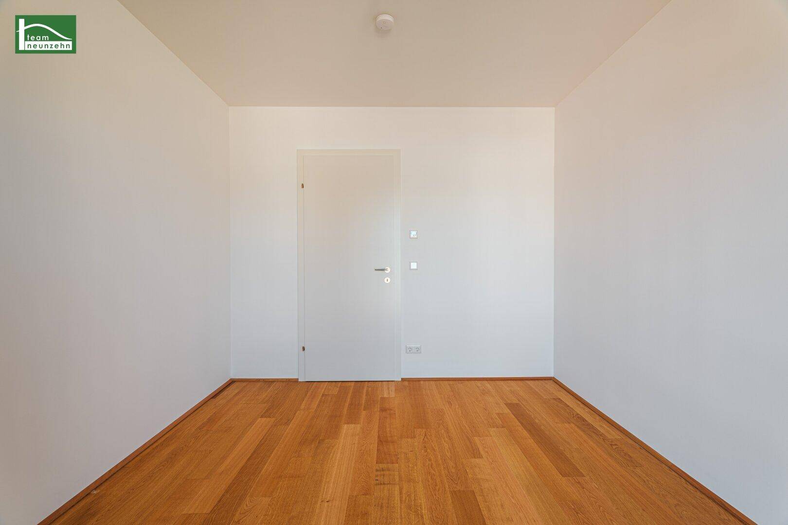 Schlichter, leerer Raum mit Holzboden und einer modernen weißen Innentür.