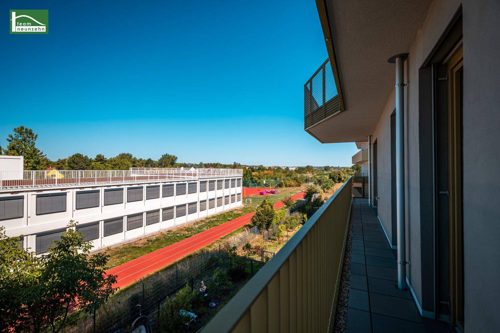 Balkon mit Fliesenboden und weitem Blick auf eine Sportanlage und die grüne Landschaft.
