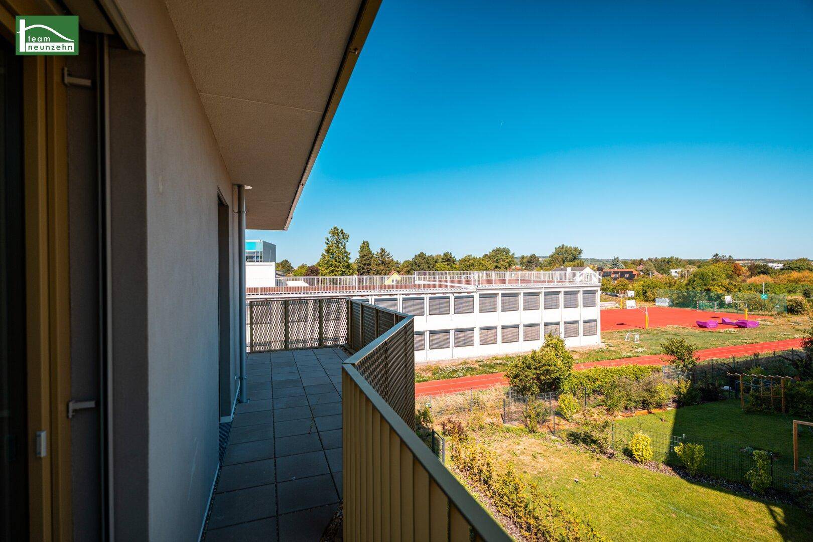 Geräumiger Balkon mit Fliesenboden und Blick auf eine Sportanlage und Grünflächen.