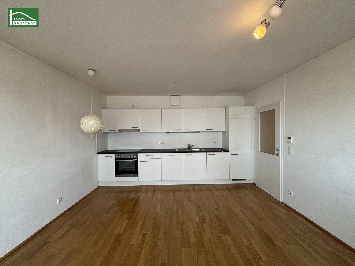 Moderne Einbauküche mit weißen Schränken und dunkler Arbeitsplatte in einem hellen Raum.