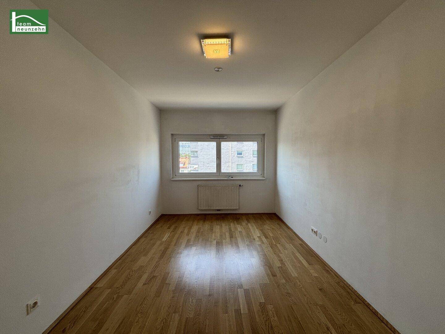 Leeres Zimmer mit Holzboden und einem Fenster, ideal als Schlaf- oder Arbeitszimmer.