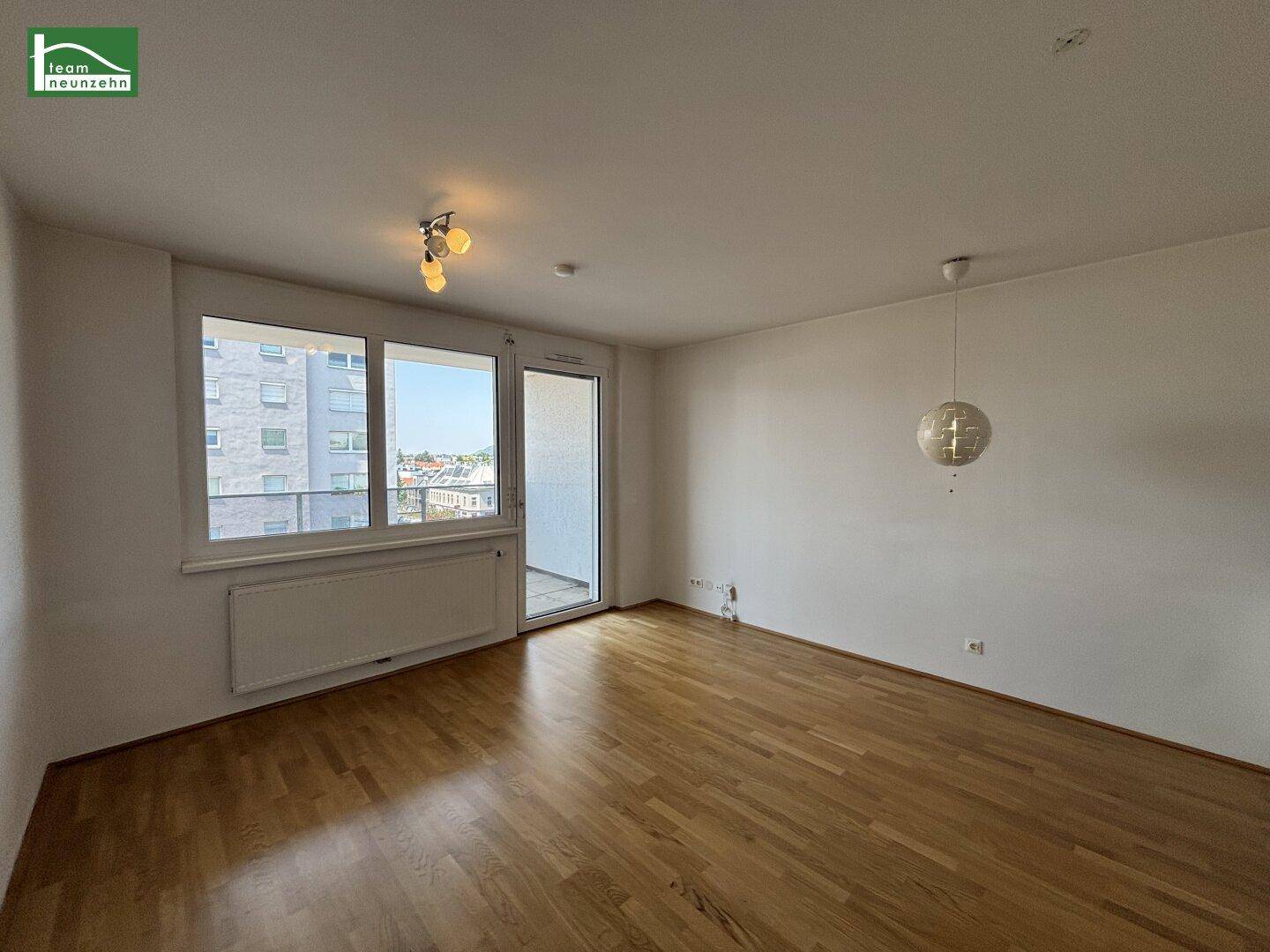 Geräumiges, leeres Wohnzimmer mit Holzboden und viel Tageslicht durch große Fenster.