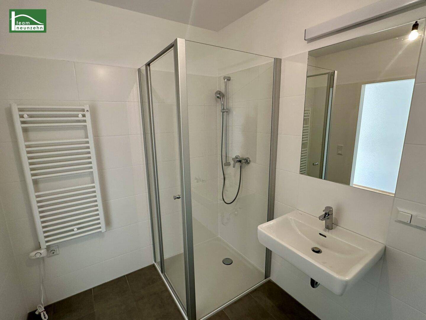 Modernes Badezimmer mit Duschkabine, Waschbecken und beheiztem Handtuchhalter.