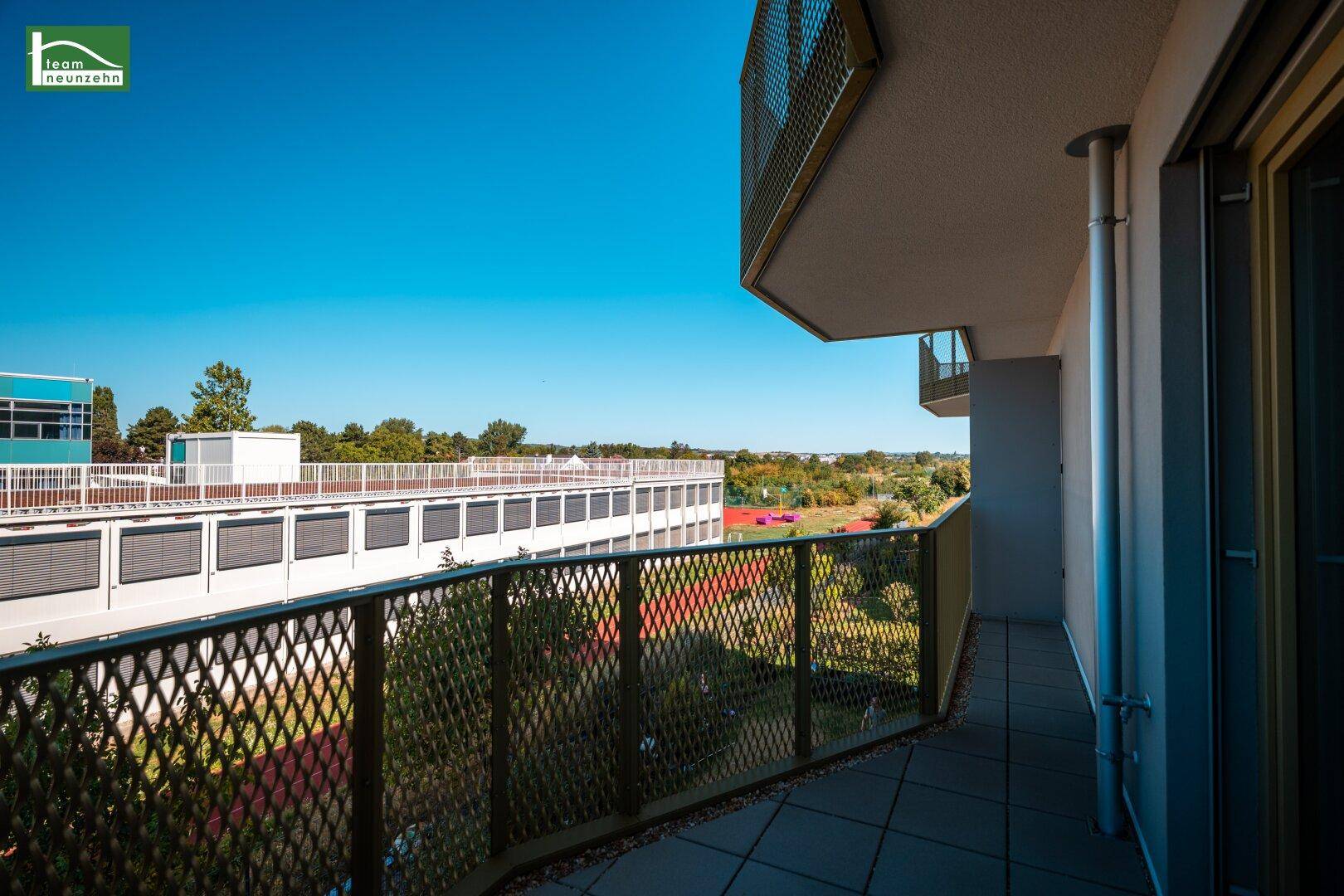 Geräumiger Balkon mit Metallgeländer und Blick auf umliegende Gebäude und Grünflächen.
