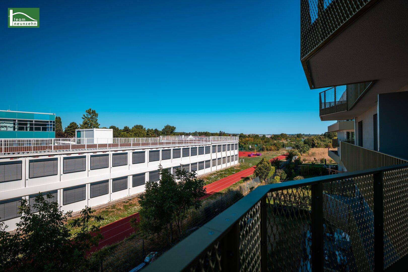 Balkon mit weitem Blick über Sportanlagen und angrenzende Gebäude unter blauem Himmel.