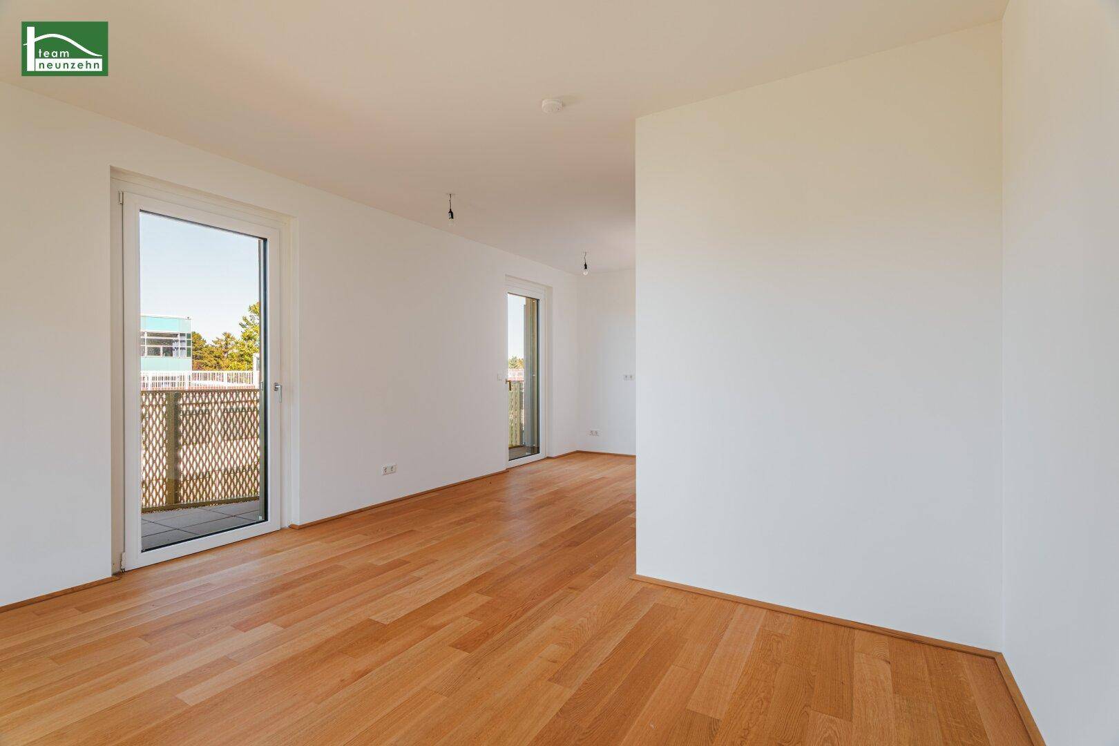 Geräumiger, heller Raum mit Holzboden und zwei Balkonzugängen, bietet viel natürliches Licht.