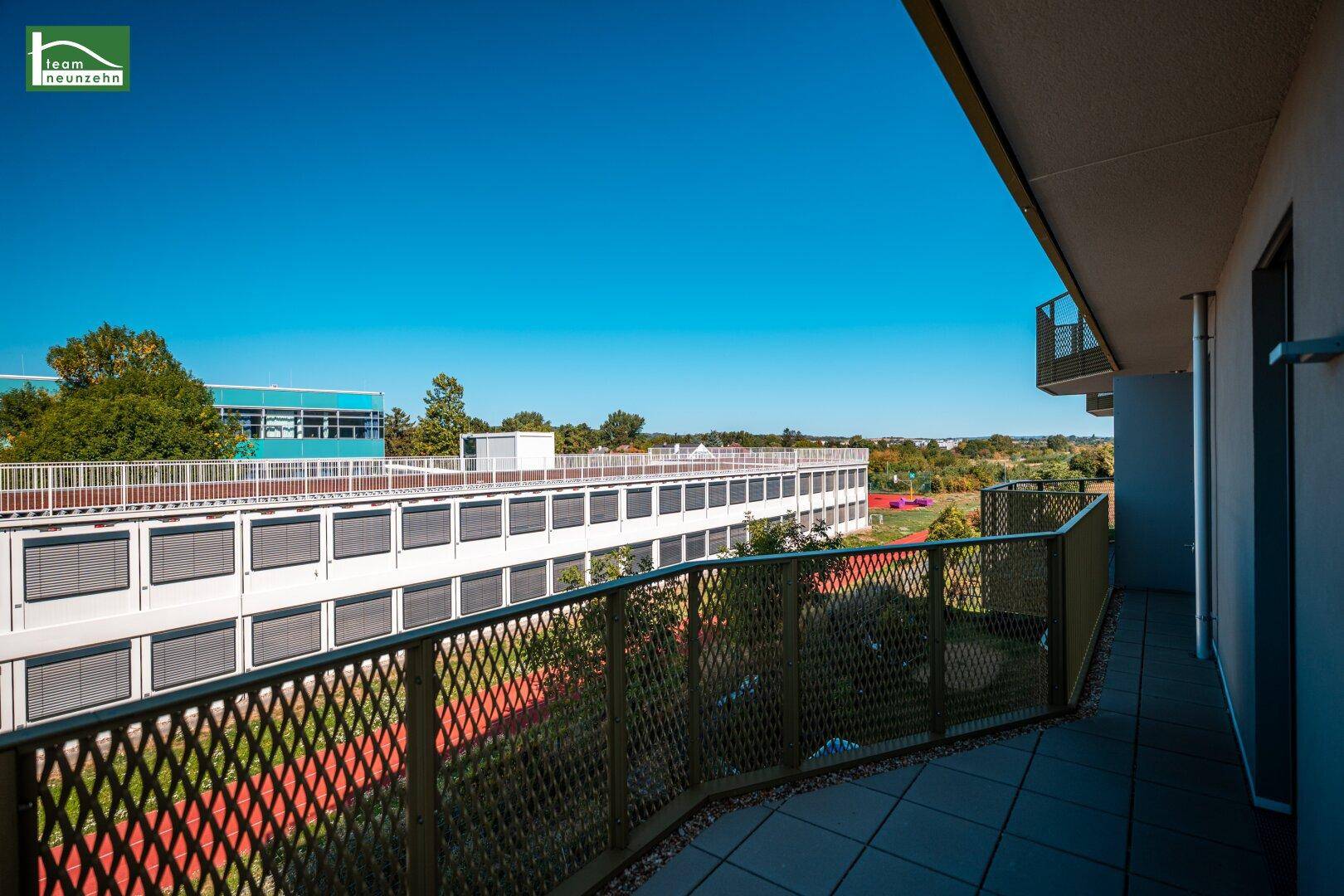 Weitläufiger Balkon mit Ausblick auf umliegende Gebäude und eine gepflegte Grünfläche.