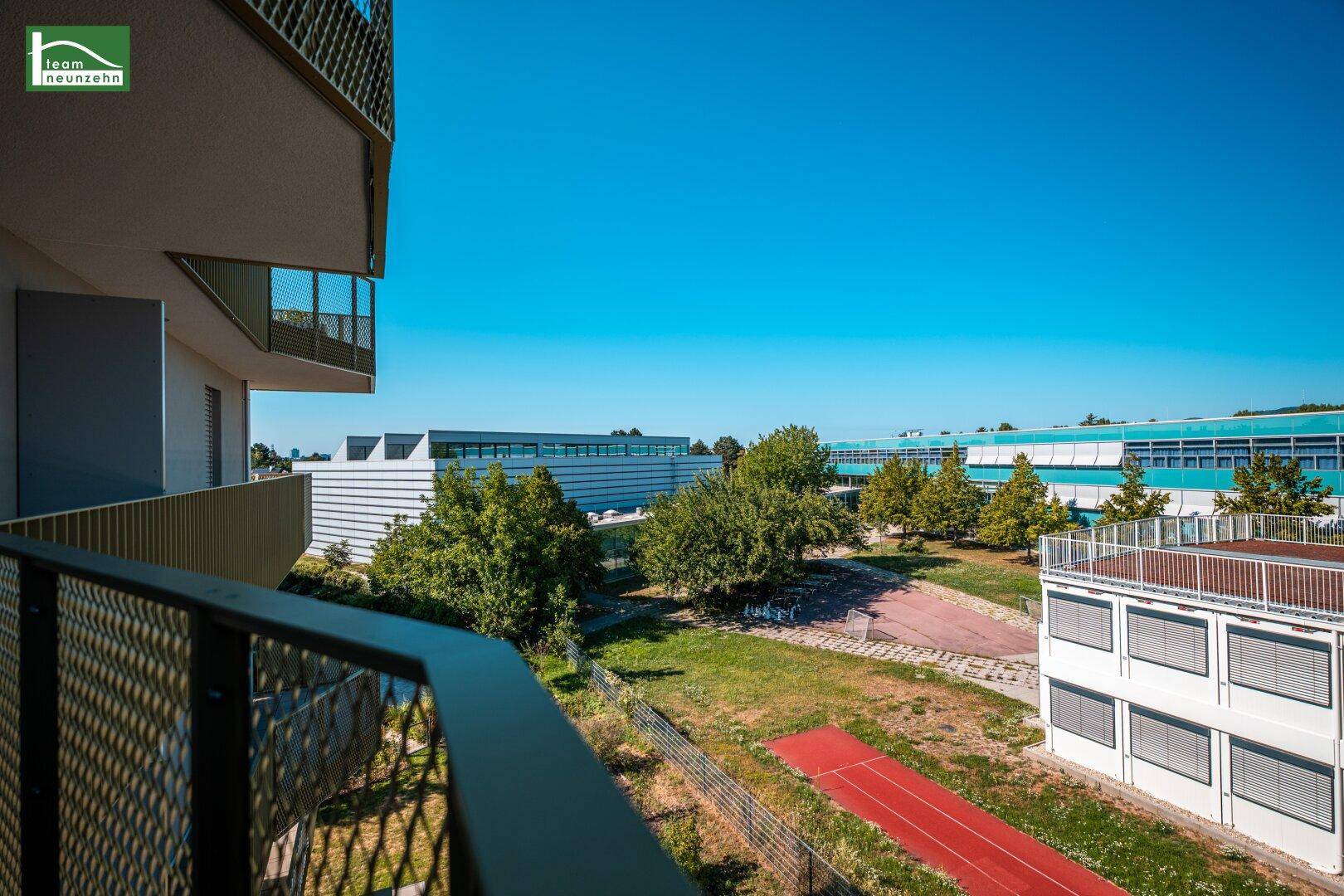 Blick vom Balkon auf einen grünen Innenhof mit Gebäuden und einer roten Laufbahn.