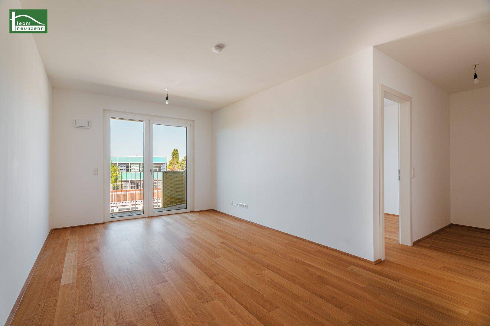 Helles, leeres Zimmer mit Holzboden und Zugang zu einem Balkon, ideal als Wohnbereich.
