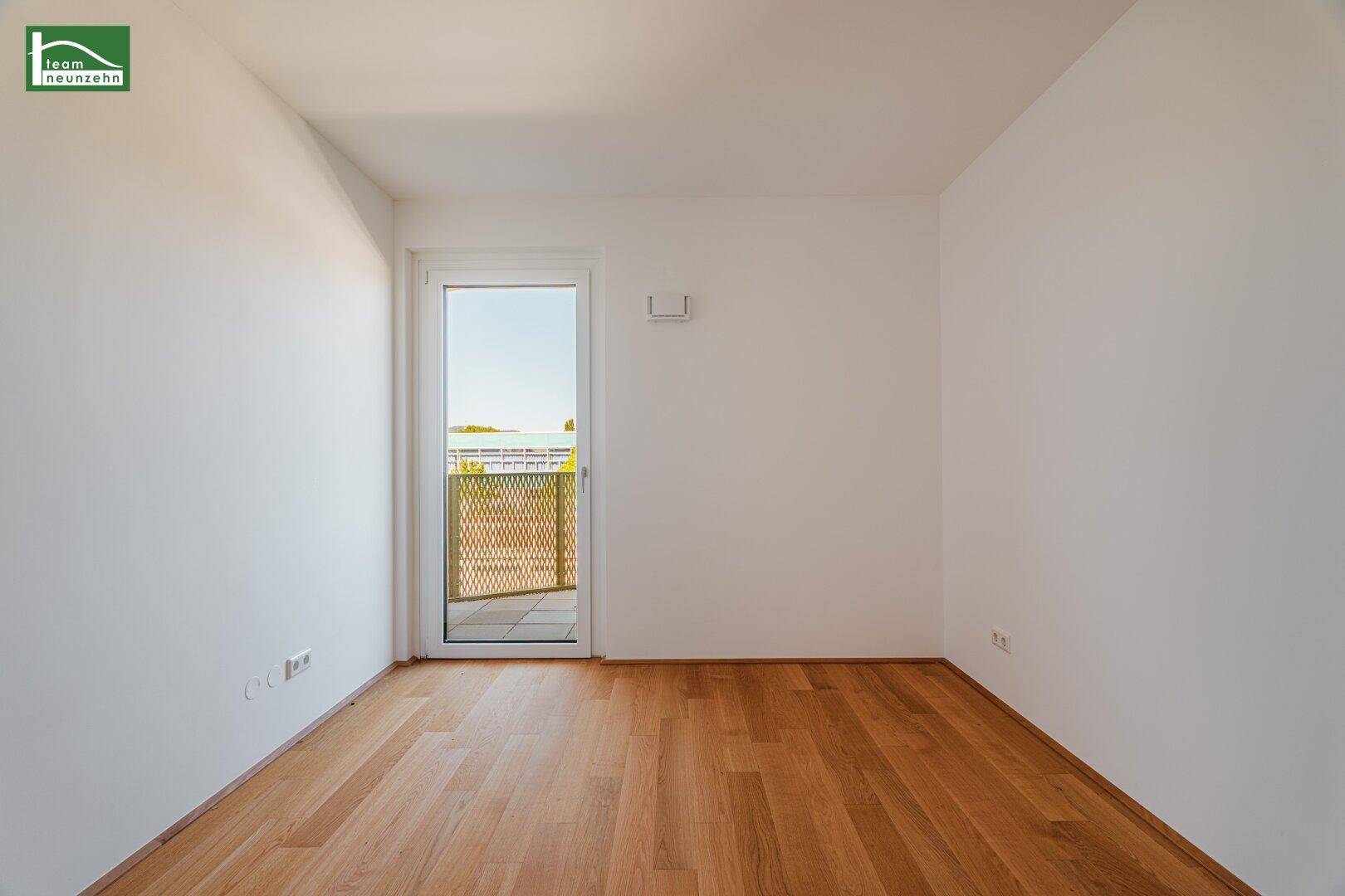 Helles Zimmer mit Holzboden und Balkonzugang, ideal als Schlaf- oder Arbeitszimmer.