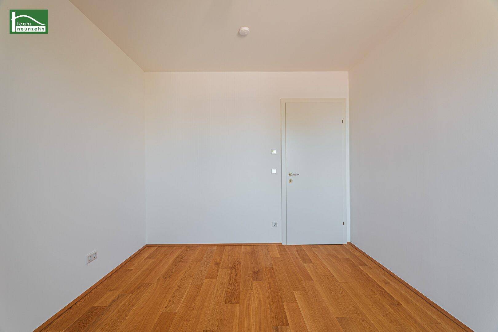 Leeres Zimmer mit Holzboden und weißer Tür, bereit für individuelle Einrichtung.