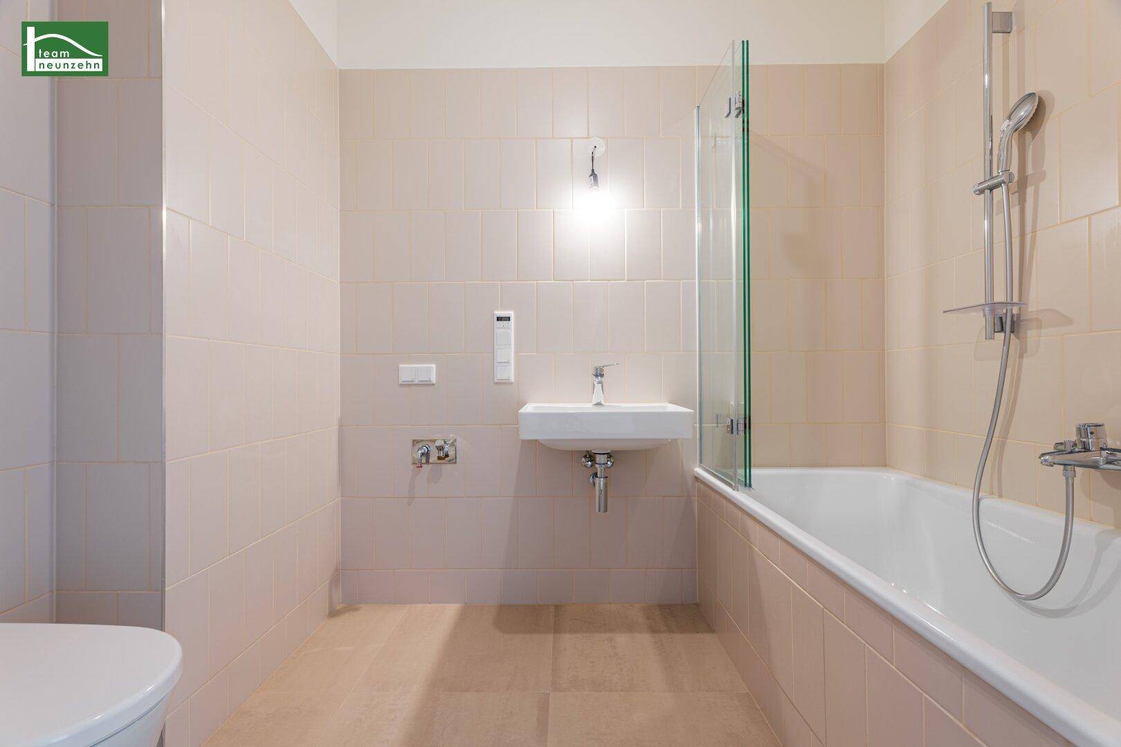 Modernes Badezimmer mit hellbeigen Fliesen, Badewanne mit Duschwand und Einzelwaschbecken.