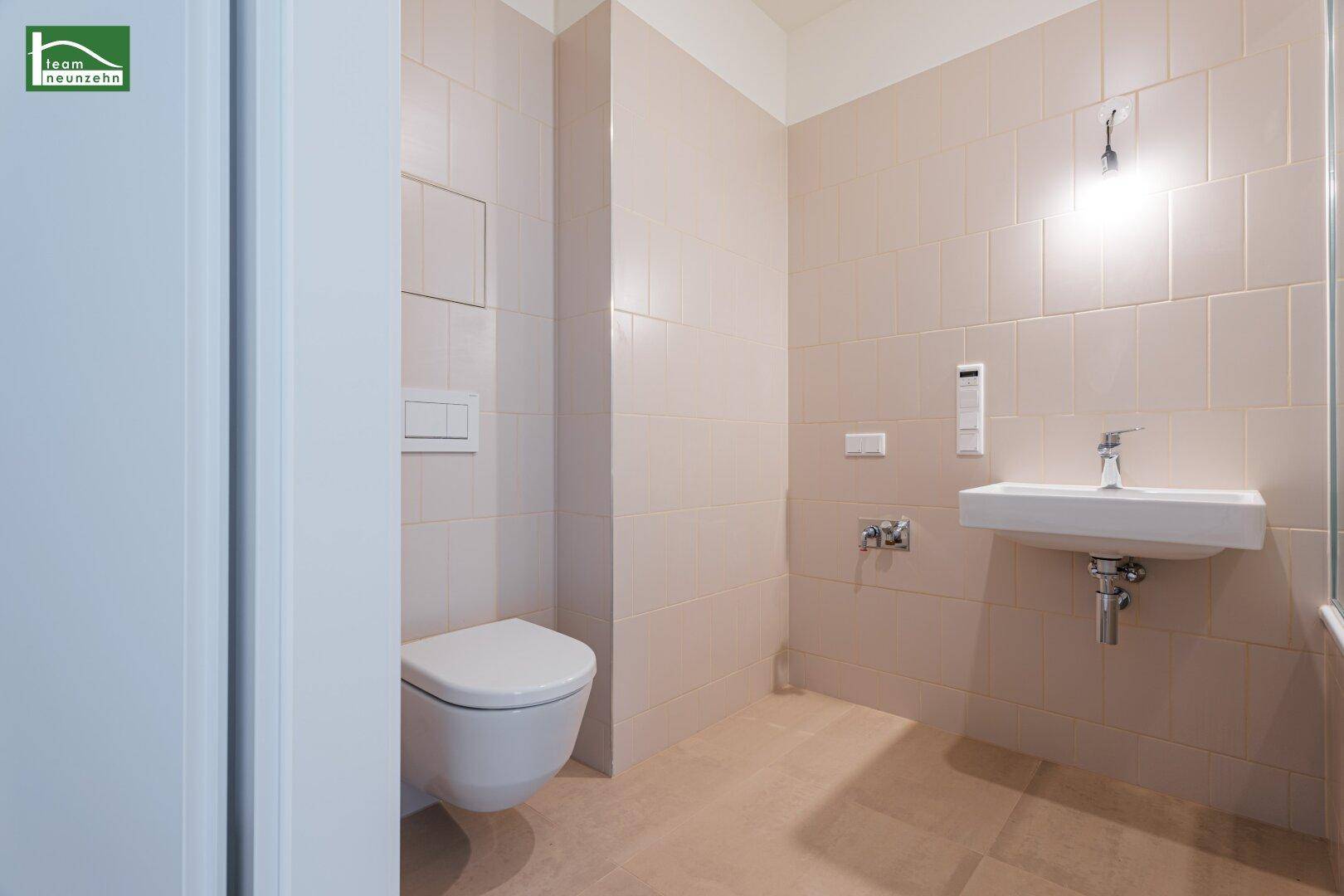Funktionales Badezimmer mit hellbeigen Fliesen, wandhängendem WC und Einzelwaschbecken.
