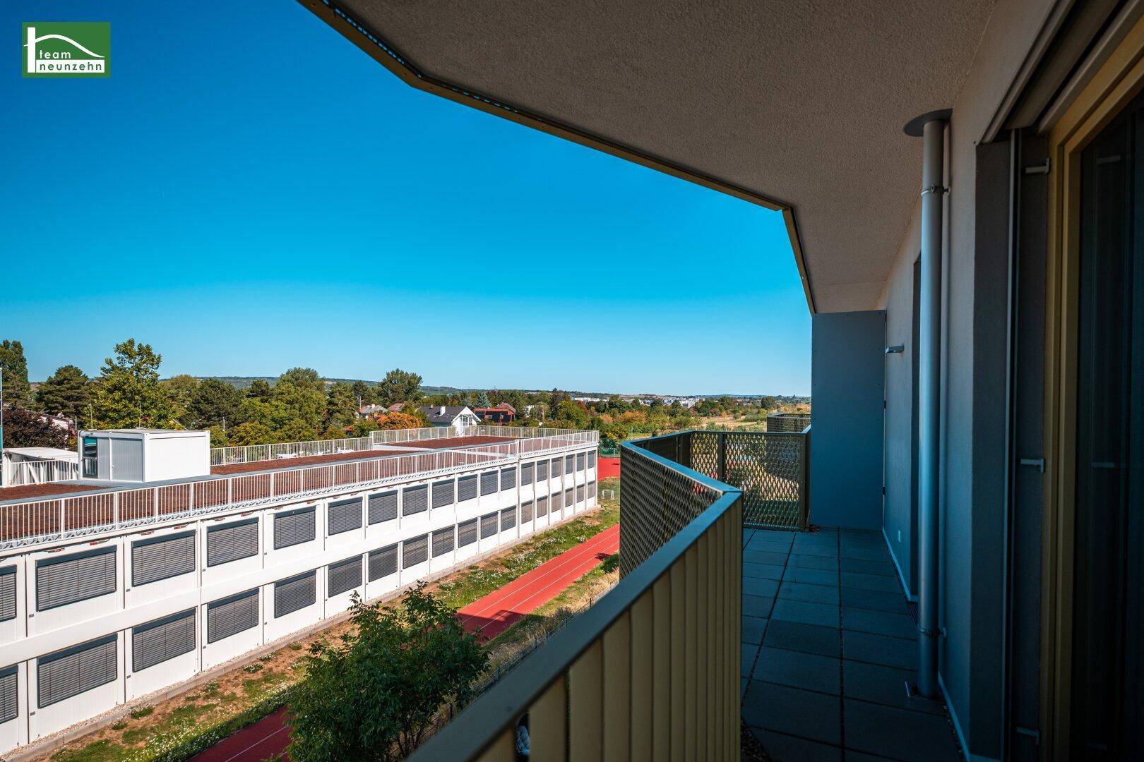 Panoramablick vom Balkon über eine Sportanlage und weite grüne Landschaft.
