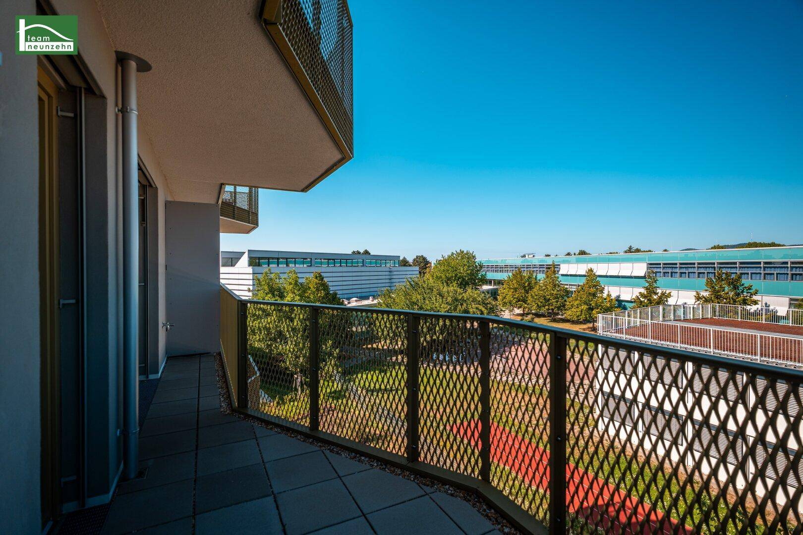 Geräumiger Balkon mit Metallgeländer und Fliesenboden, bietet Blick auf einen grünen Innenhof.