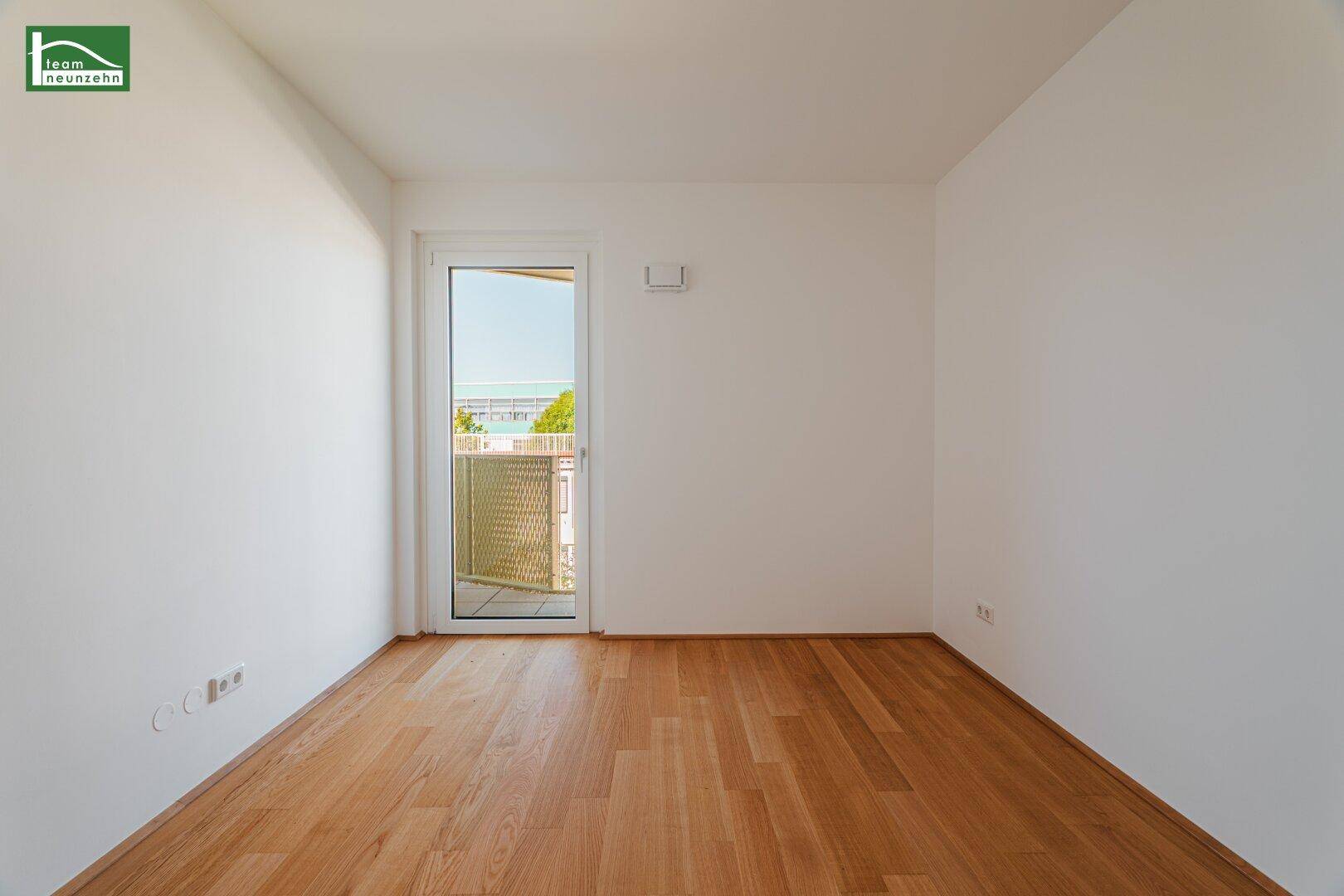 Leeres Schlafzimmer mit Holzboden und Balkontür, bietet viel natürliches Licht und frische Luft.