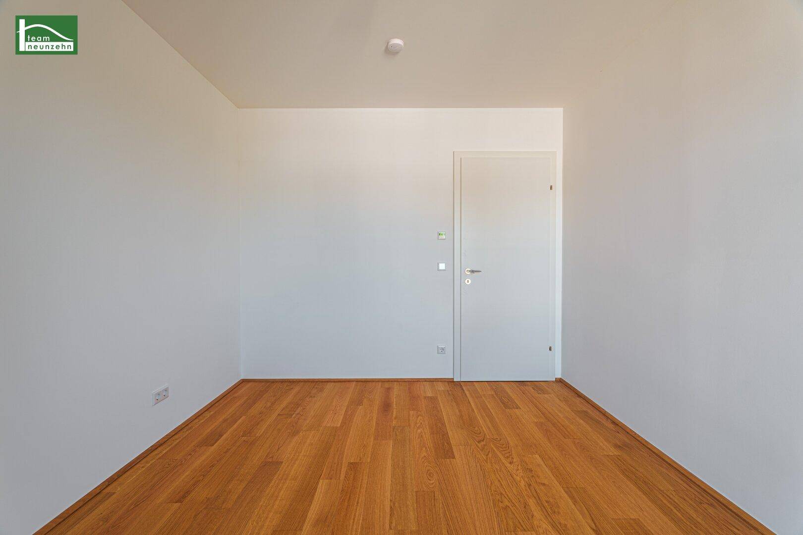 Helles, leeres Zimmer mit Holzboden und weißer Tür, ideal als Schlaf- oder Arbeitszimmer nutzbar.