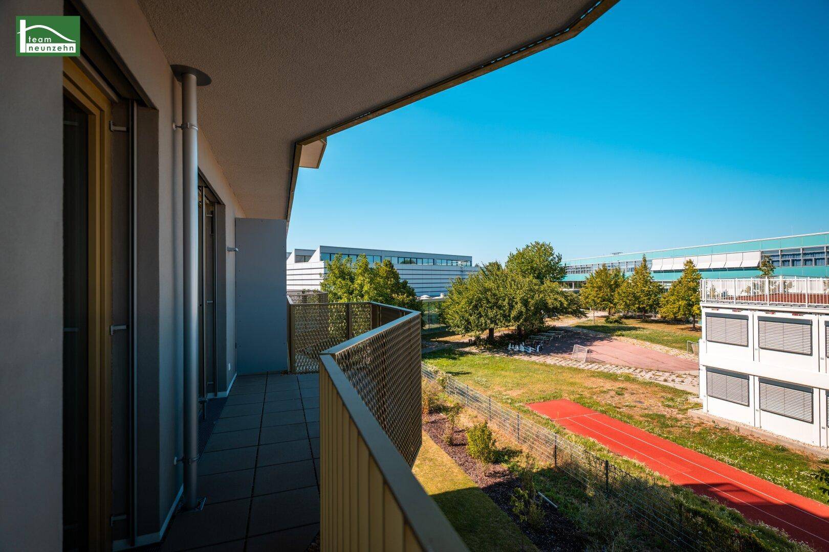 Heller Balkon mit Fliesenboden und Blick auf eine gepflegte Grünfläche und moderne Gebäude.