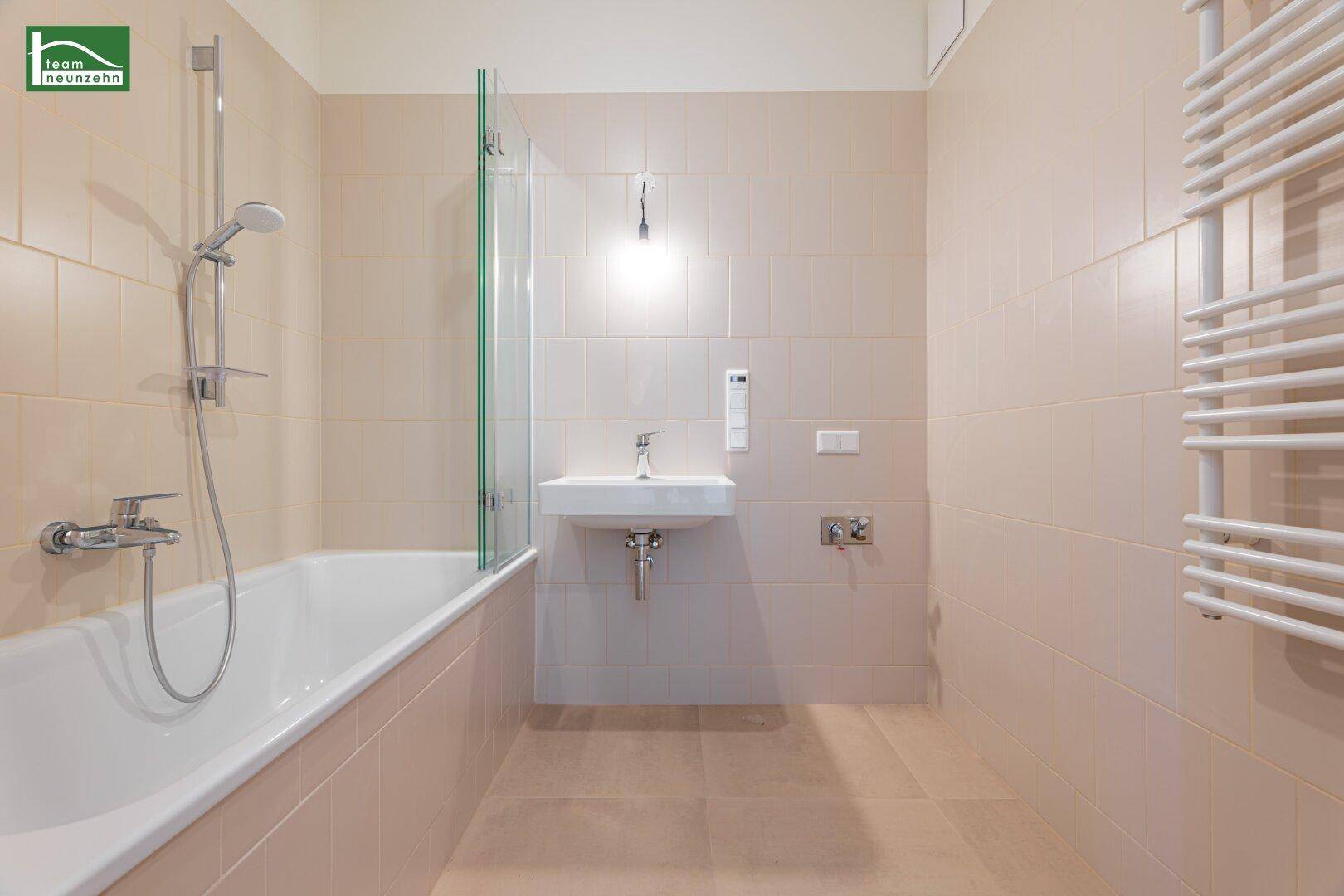 Modernes Badezimmer mit beigefarbenen Fliesen, Badewanne mit Duschfunktion und Handtuchheizkörper.