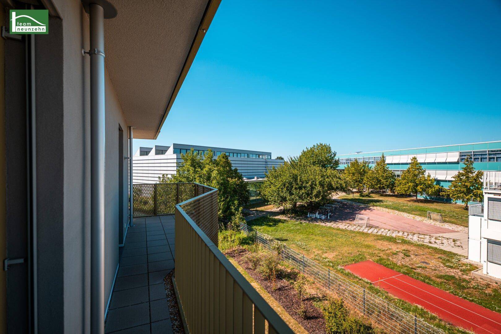 Langer Balkon mit Blick auf eine grüne Anlage und Sportplätze, ideal zum Entspannen.