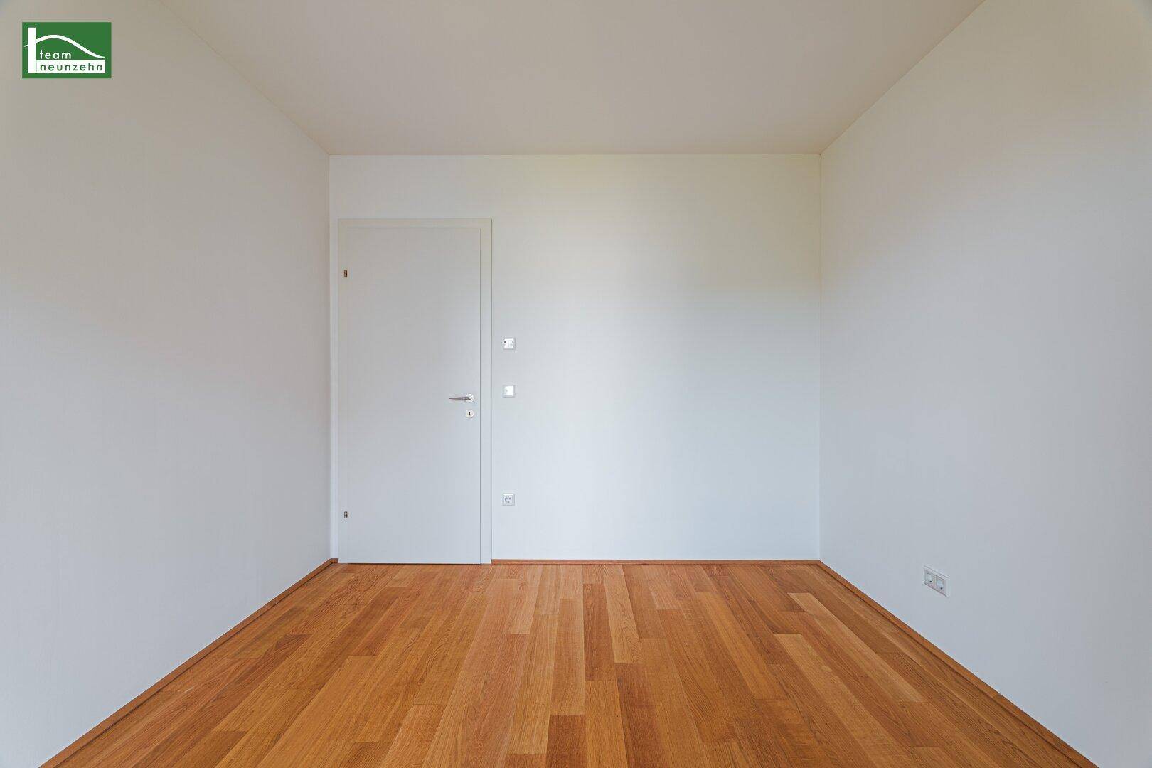 Leeres Zimmer mit Holzboden und weißer Tür, bereit für individuelle Gestaltung.