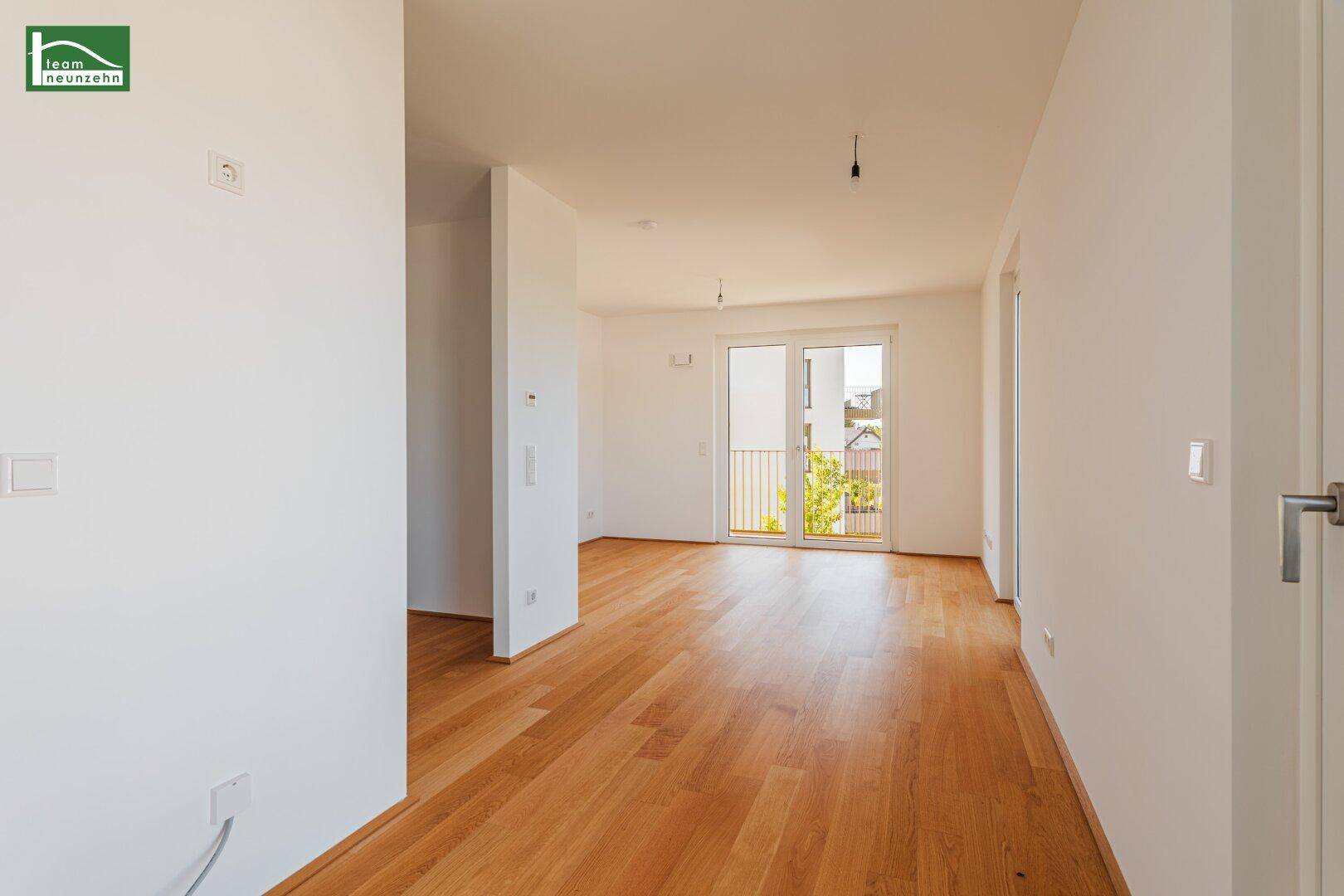 Helles, leeres Zimmer mit Holzboden und Zugang zu einem Balkon, ideal für einen Wohnbereich.