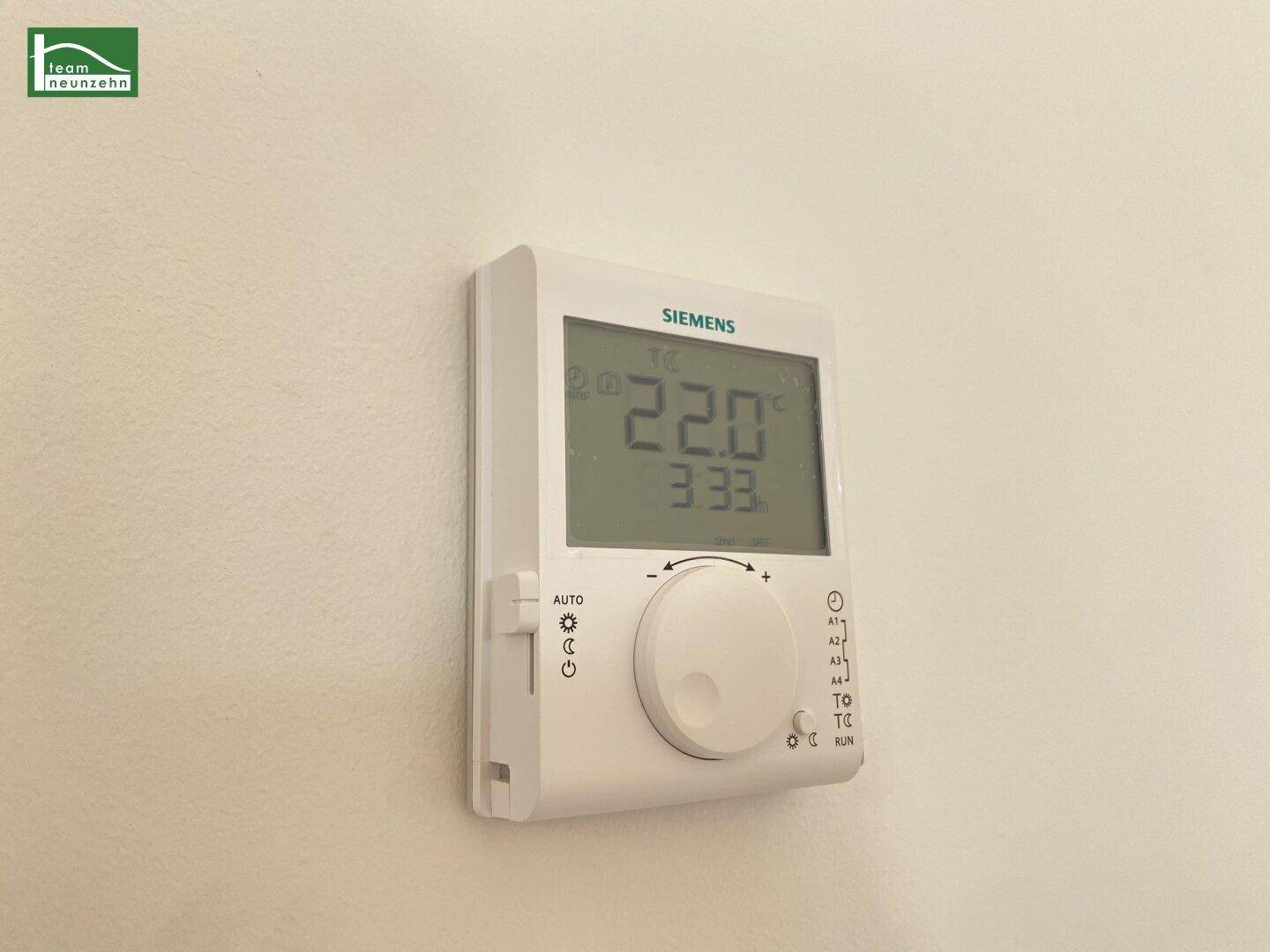 Digitaler Siemens-Thermostat zur Temperaturregelung an einer weißen Wand montiert.